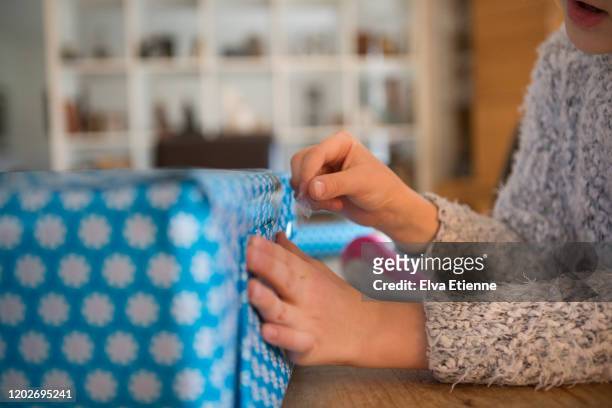 close-up of a child using adhesive tape to secure blue wrapping paper on a gift - tape dispenser fotografías e imágenes de stock