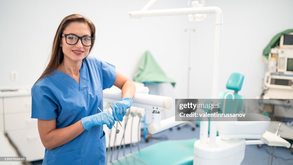 Retrato de dentista femenino, sosteniendo la herramienta dental y de pie en su oficina