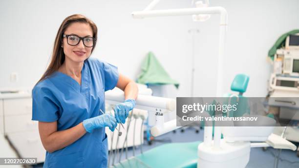 portrait of female dentist,holding dental tool and standing at her office - dental hygienist stock pictures, royalty-free photos & images