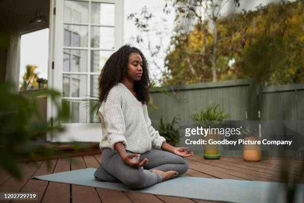young woman sitting in the lotus pose outside on her patio - meditation stock pictures, royalty-free photos & images
