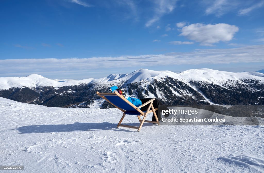 Woman sitting in a chair in snow, enjoying the winter sun, Après-ski lounge at the top of Turracher Höhe, Austria.