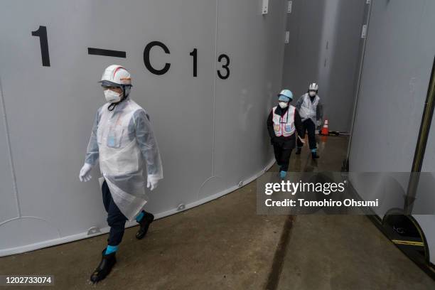 Members of the media and Tokyo Electric Power Co. Employees walk past storage tanks for radioactive water at the Fukushima Dai-ichi nuclear power...