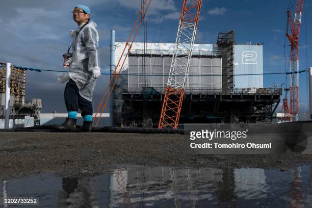 An employee walks past the Unit 2 reactor building at Tokyo Electric Power Co.'s Fukushima Dai-ichi nuclear power plant on January 29, 2020 in Okuma,...