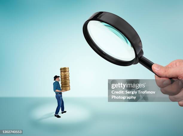 man holding a stack of coins and big magnifying glass in hand - tax fraud 個照片及圖片檔