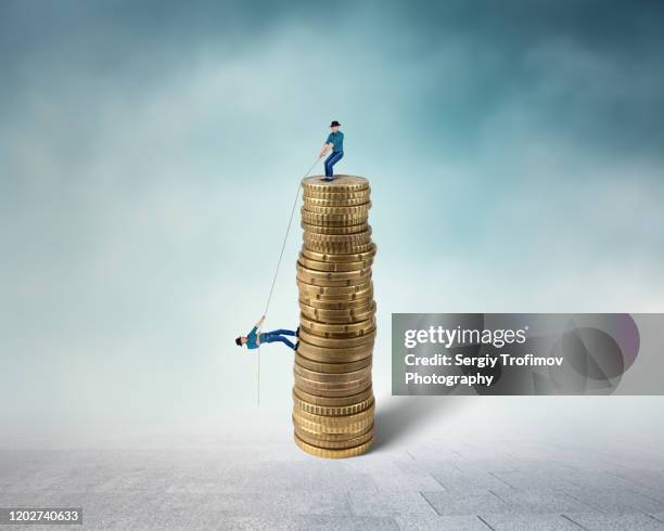 man helping friend to climb the top of coins stack with a rope - equal pay stock-fotos und bilder