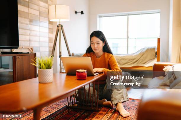 giovane donna che usa il laptop comodamente a casa - young people looking at camera foto e immagini stock