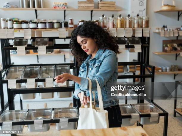 jonge vrouw die herbruikbare winkelende zak in opslag gebruikt - beauty shopping stockfoto's en -beelden