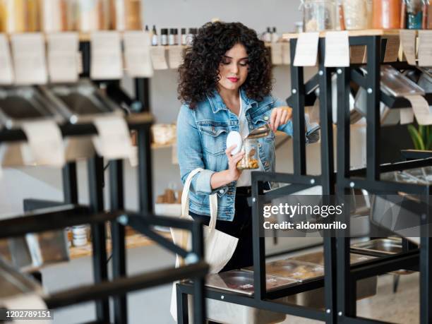 pretty young woman filling jar in zero waste store - filling jar stock pictures, royalty-free photos & images