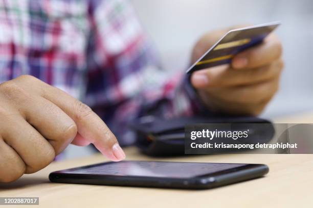 closeup young man hands holding credit card and using cell, smart phone for online shopping or reporting lost card, fraudulent transaction - fraud photos et images de collection