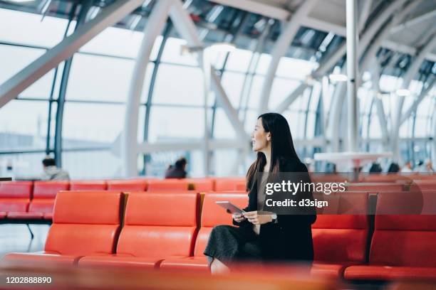 smiling young asian woman reading on digital tablet while waiting for her flight in airport lounge - business class flight stockfoto's en -beelden