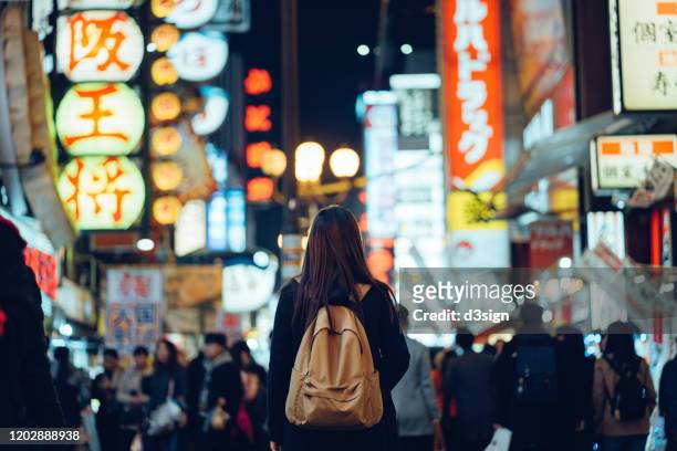 young asian female traveller exploring and strolling along the busy and colourful neon signboard downtown city street at night in osaka, japan - giappone foto e immagini stock