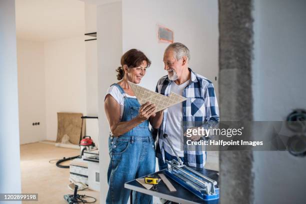 senior couple laying tile floor in new home, using manual cutter. - working on the move stock pictures, royalty-free photos & images