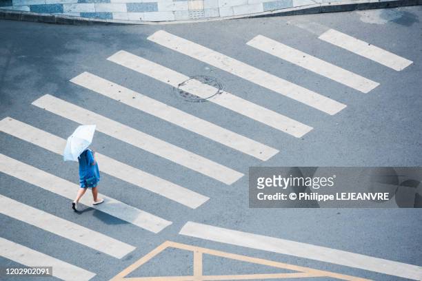 woman with a blue umbrella walking on a crosswalk - umbrellas from above photos et images de collection