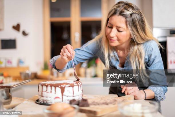 mulher assando em casa: decorar bolo de esponja de chocolate - decorating a cake - fotografias e filmes do acervo