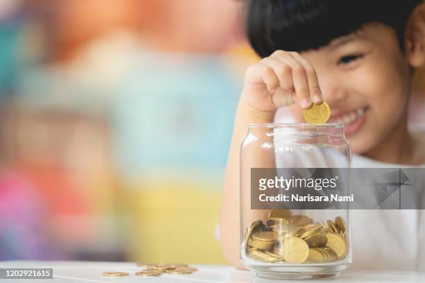 kid dropping coins into the glass for saving the money. selective focu - numismatik stock-fotos und bilder