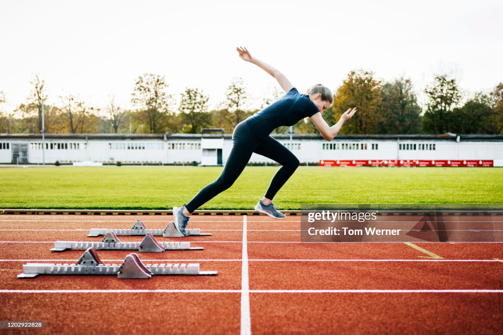 Woman Sprinting Off Start Line On Outdoor Running Track