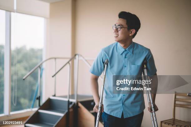 een aziatische chinese mannelijke patiënt die van zijn beenverwonding herstelt en met krukken in het ziekenhuis loopt - crutches stockfoto's en -beelden