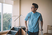 an asian chinese male patient recovering from his leg injury and walking with crutches in the hospital