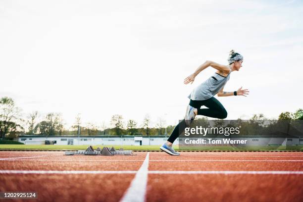 woman sprinting off starting blocks on outdoor running track - leichtathletik stock-fotos und bilder