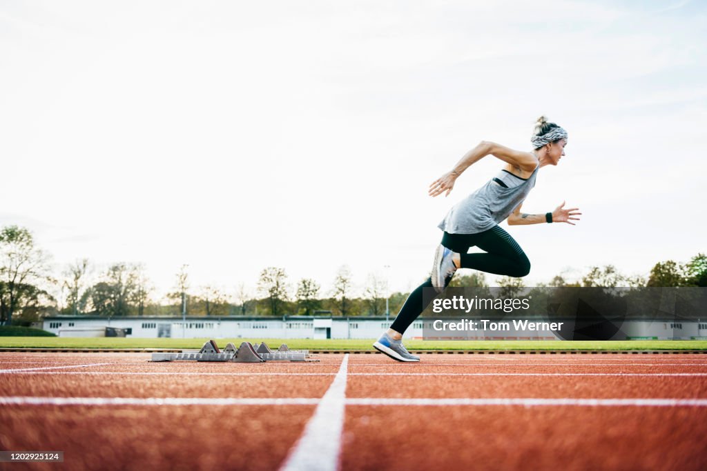 Woman Sprinting Off Starting Blocks On Outdoor Running Track