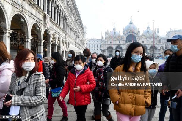 Tourists wearing protective facemasks visit the Piazza San Marco, in Venice, on February 24, 2020 during the usual period of the Carnival festivities...