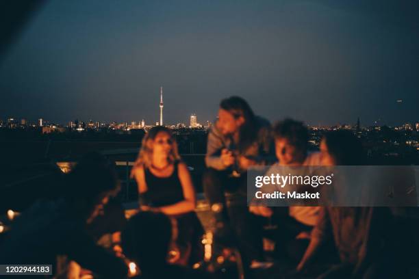 friends enjoying on terrace against cityscape at dusk - berlin night stock-fotos und bilder