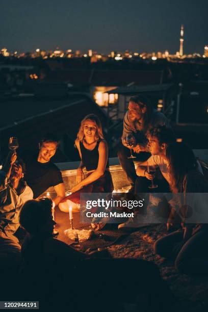 high angle view of friends enjoying rooftop party on illuminated terrace in candlelight - rooftop party night stock pictures, royalty-free photos & images