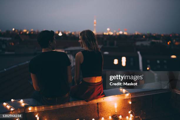 rear view of young couple sitting on illuminated terrace in city at dusk - low key beleuchtung stock-fotos und bilder