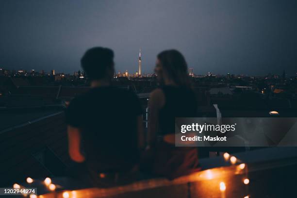 rear view of couple sitting on terrace against cityscape at dusk - alexanderplatz stock-fotos und bilder