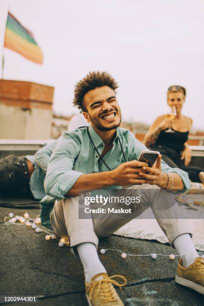 cheerful young man text messaging on smart phone while enjoying party on terrace - millennials at party photos et images de collection