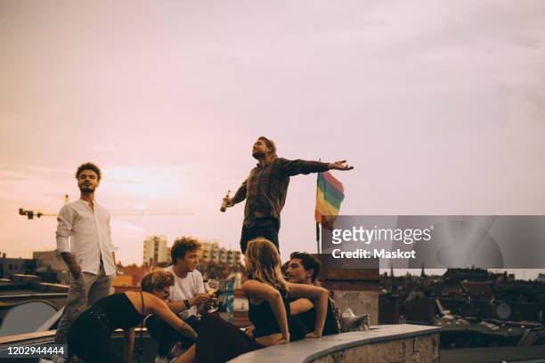 man enjoying beer while relaxing with friends on terrace at rooftop party - millennials at party photos et images de collection