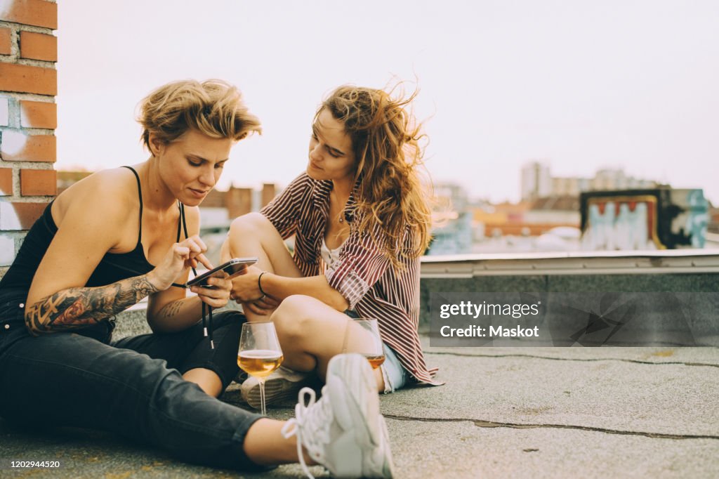 Woman showing mobile phone to friend while sitting on terrace during rooftop party