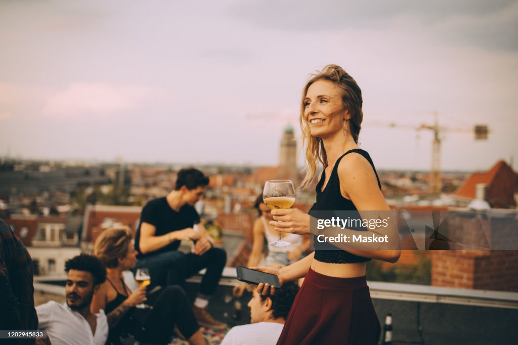 Smiling woman enjoying drink while partying with friends at rooftop