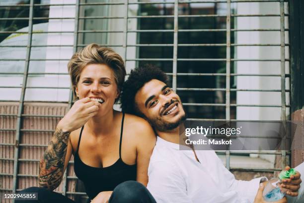 portrait of woman eating fruit while friend leaning on her against window - fashion food stock pictures, royalty-free photos & images