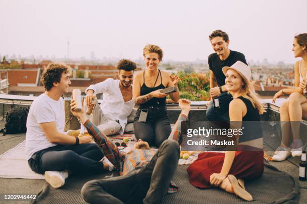 friends enjoying music on speaker during rooftop party at terrace against sky - freundschaft stock-fotos und bilder