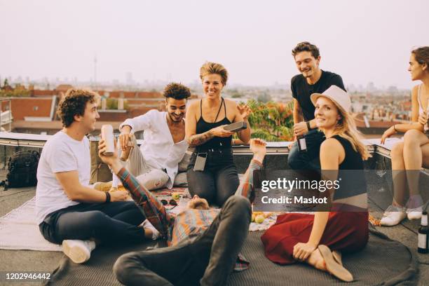 friends enjoying music on speaker during rooftop party at terrace against sky - portable speaker stock pictures, royalty-free photos & images
