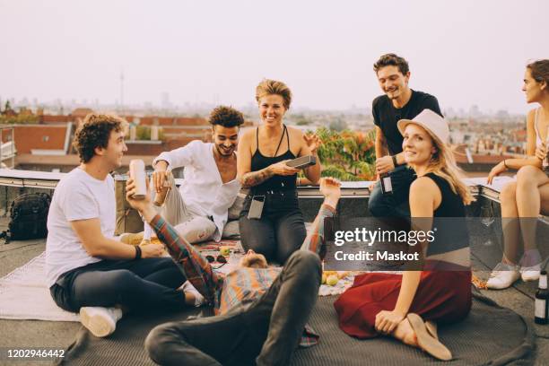 friends enjoying music on speaker during rooftop party at terrace against sky - portability stock pictures, royalty-free photos & images