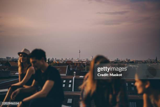 friends talking while sitting on terrace during rooftop party in city at dusk - mitte photos et images de collection