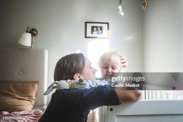 father consoling crying blond baby boy in crib with tender love at home - baby father hug side stock-fotos und bilder