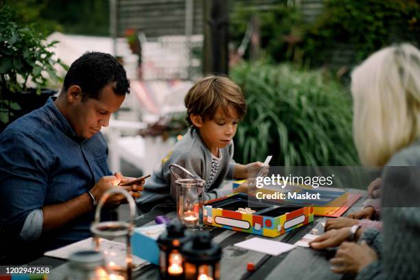 family playing board game on table while father using mobile phone - family game stock-fotos und bilder