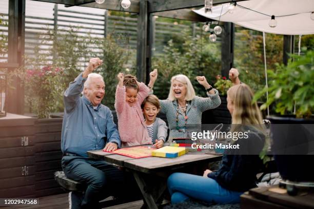 cheerful family playing board game while sitting at table in backyard - family game stock-fotos und bilder