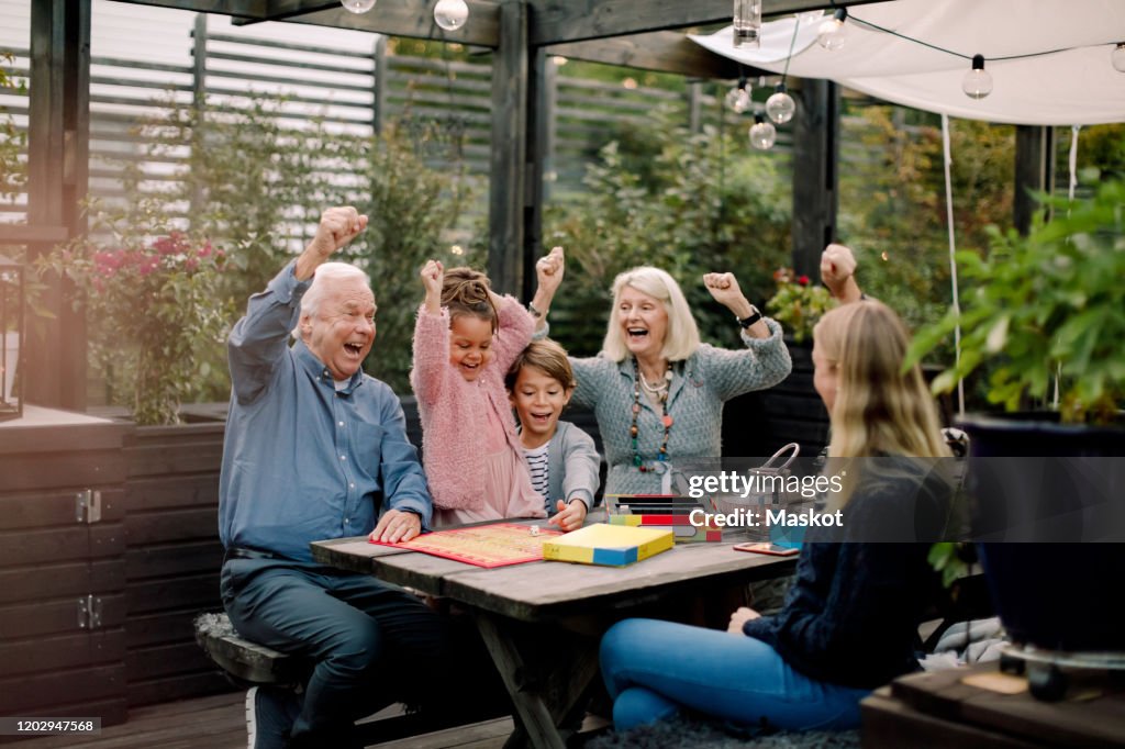 Cheerful family playing board game while sitting at table in backyard