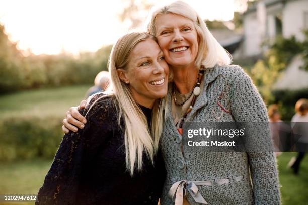 smiling senior woman and daughter standing with arm around in backyard - daughter stockfoto's en -beelden