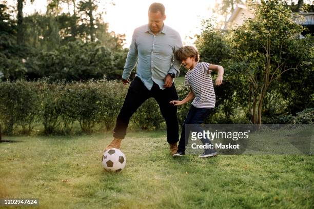 full length of father and son playing soccer in backyard during weekend activities - football player stock-fotos und bilder