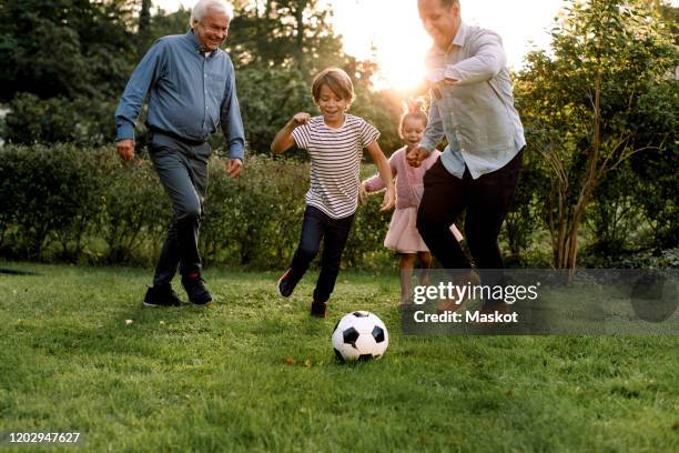 full length of multi-generation family playing soccer in backyard - jugador futbol fotografías e imágenes de stock