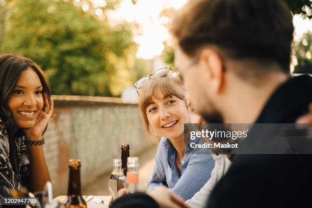 smiling women sitting by male friends at garden party - biergarten stock-fotos und bilder