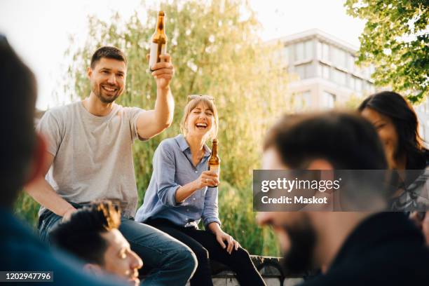male and female friends laughing while sitting at social gathering - biergarten stockfoto's en -beelden