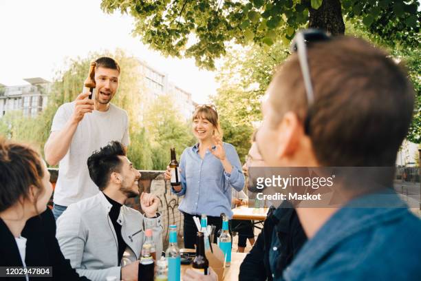 male and female friends laughing while sitting at social gathering - biergarten stock-fotos und bilder