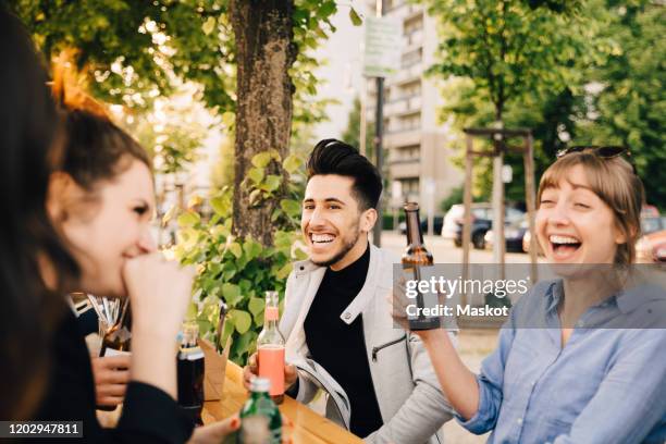 male and female friends laughing while sitting with drinks at garden party - biergarten stock-fotos und bilder