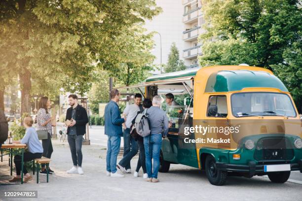 male and female customers standing by food truck - furgone ambulante foto e immagini stock